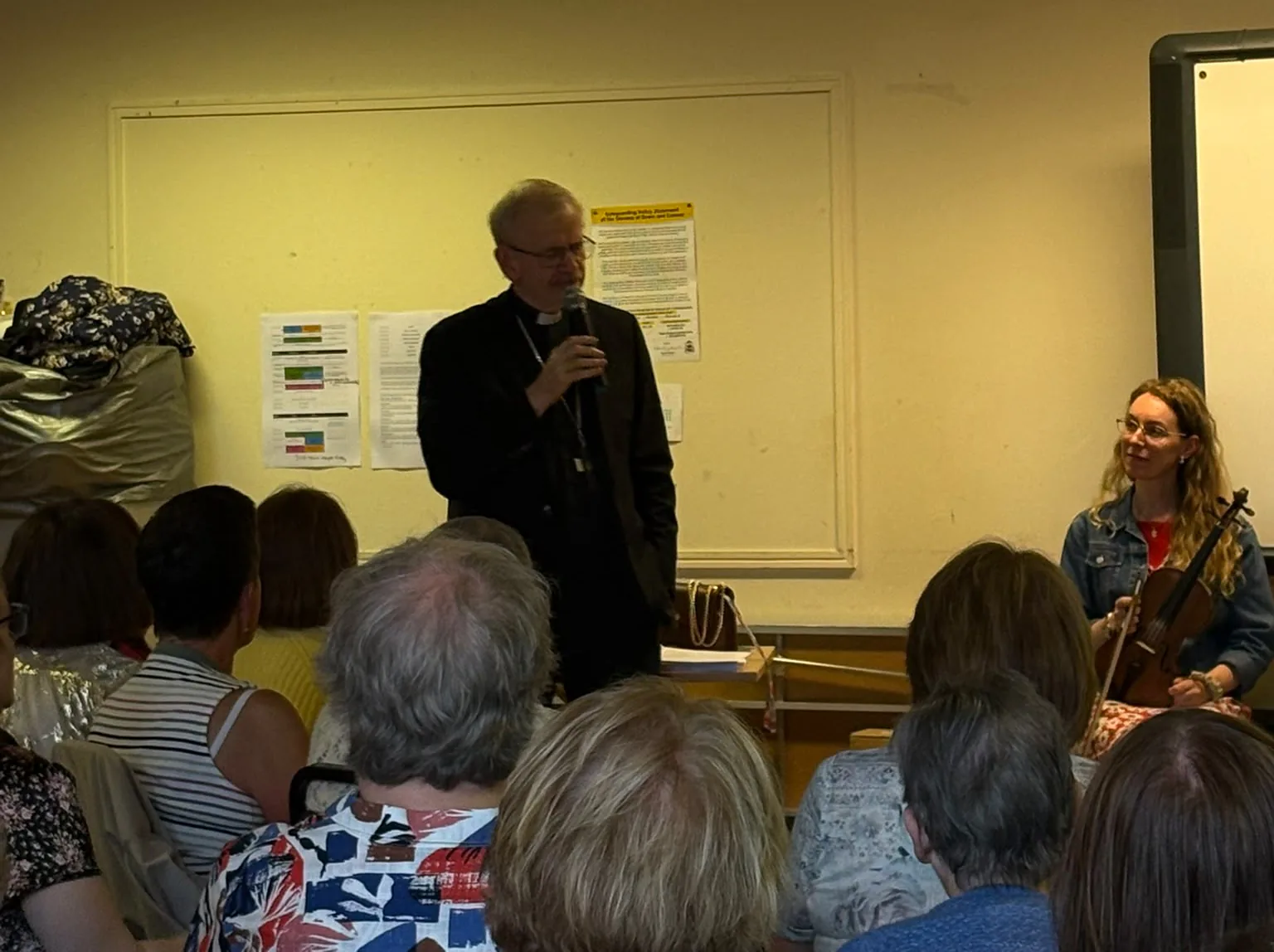 Bishop Alan McGuckian at the microphone, a fiddle player waiting beside him