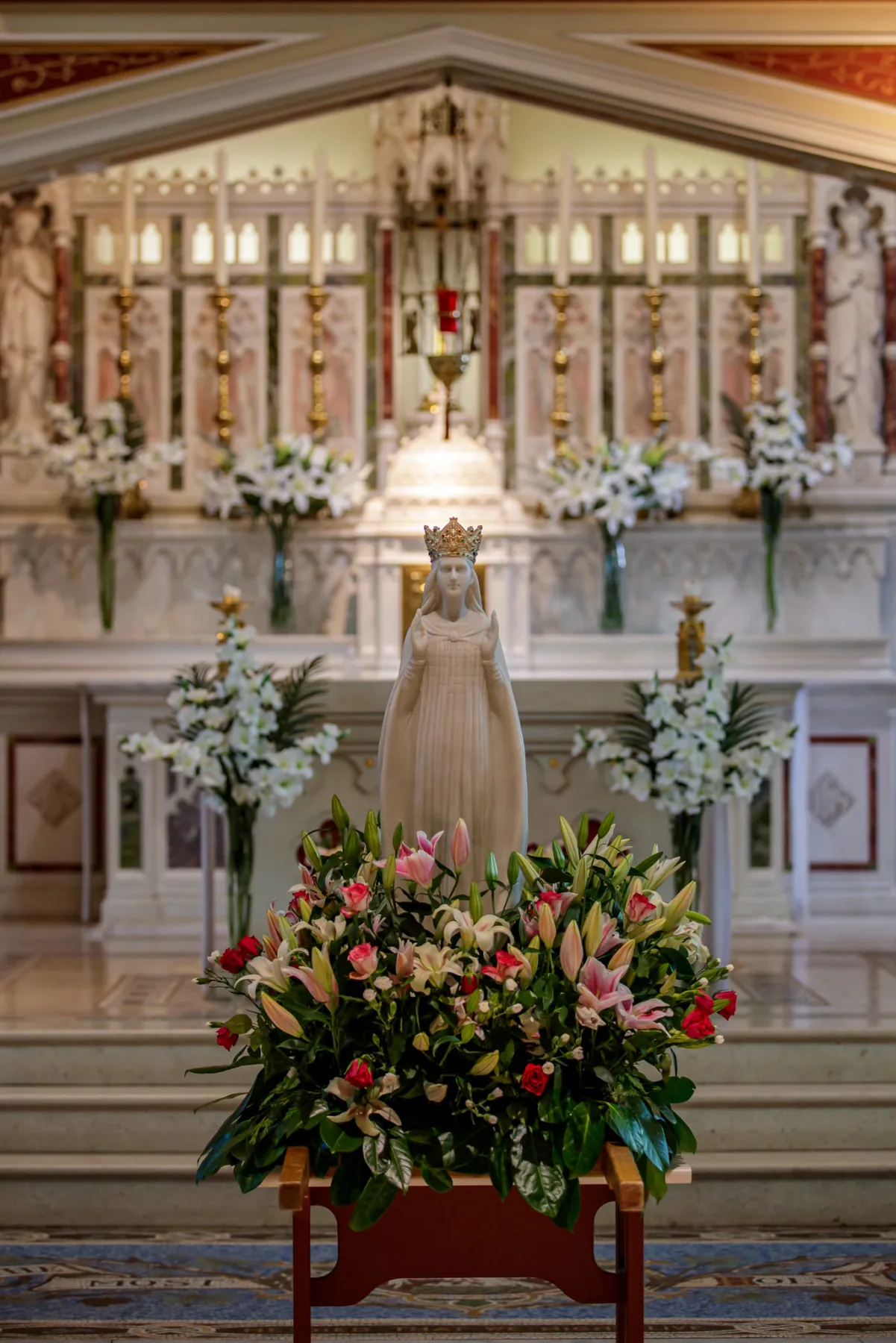 The crowned statue of Our Lady on a bed of lilies and roses before the high altar