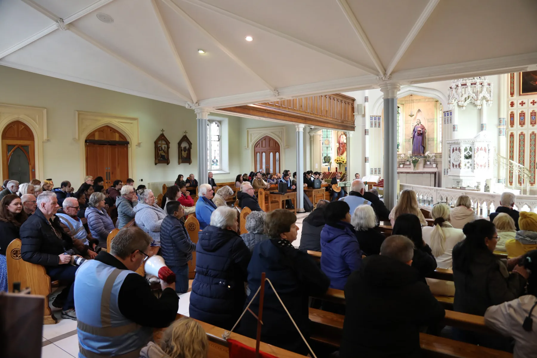 A full church, with a steward in a high-visibility vest at the end of a pew
