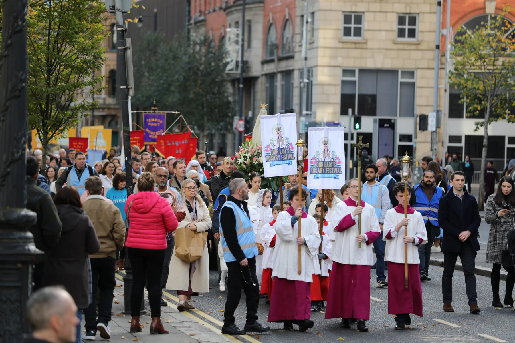 The procession turning a corner in the city centre, the altar servers and banners at its head