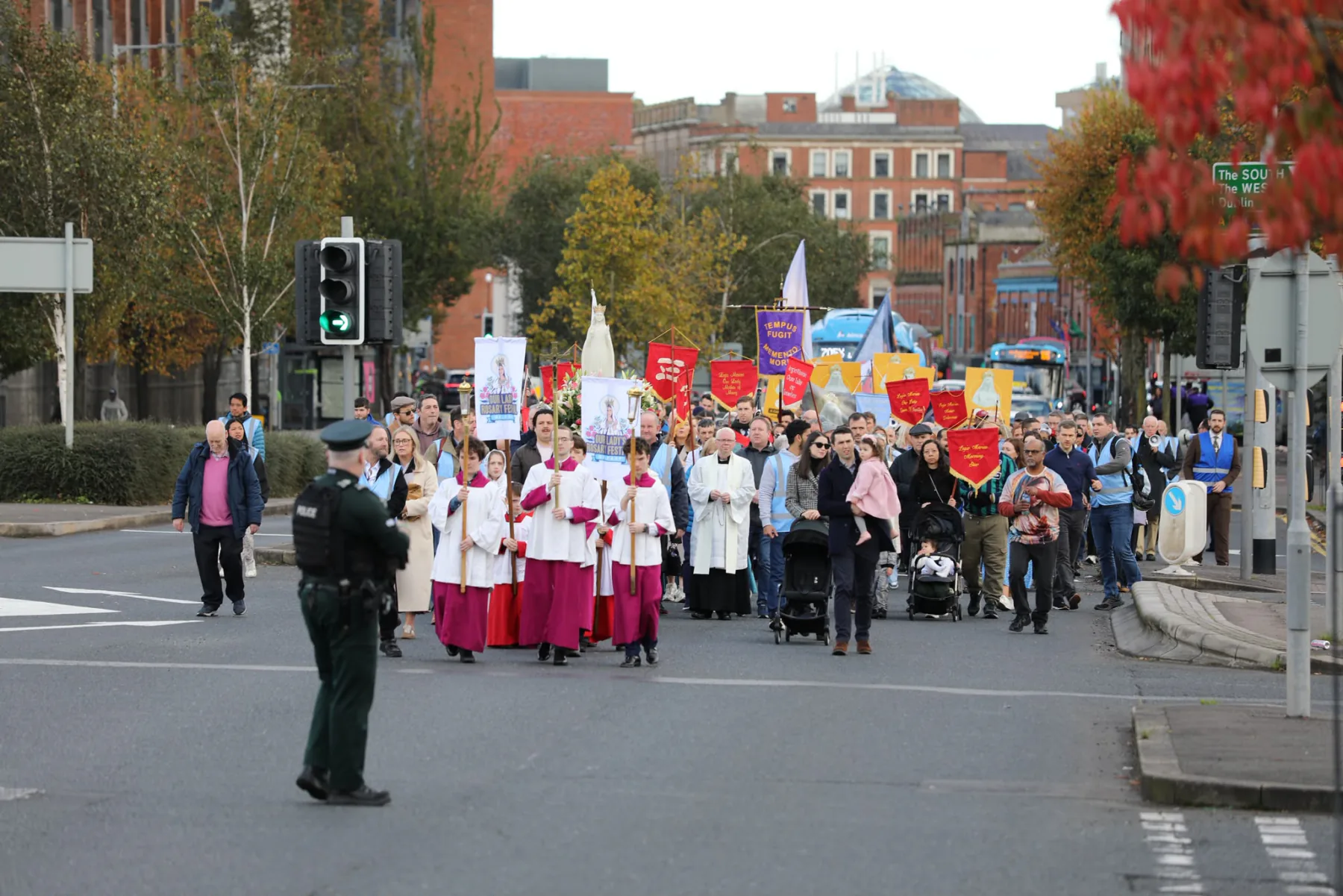 The procession coming down a wide city street, with a police officer holding the junction