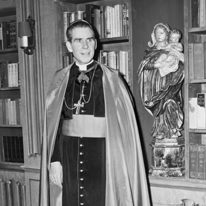 Archbishop Fulton J. Sheen in cape and pectoral cross, standing beside a statue of Our Lady and the Child Jesus