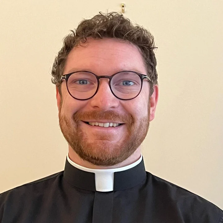 Fr John O&rsquo;Laverty, wearing a clerical collar and glasses, smiling at the camera