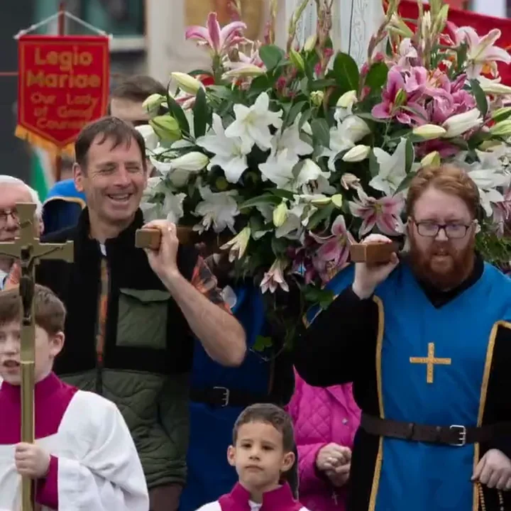 Men carrying the statue of Our Lady of F&aacute;tima on a bed of lilies beneath a Legio Mariae banner, with altar servers beside them