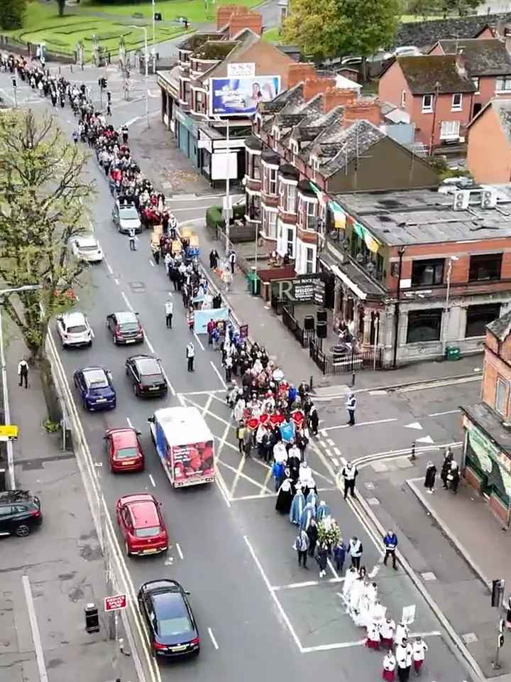A long line of people walking the Rosary Procession through the streets of Belfast, seen from above.